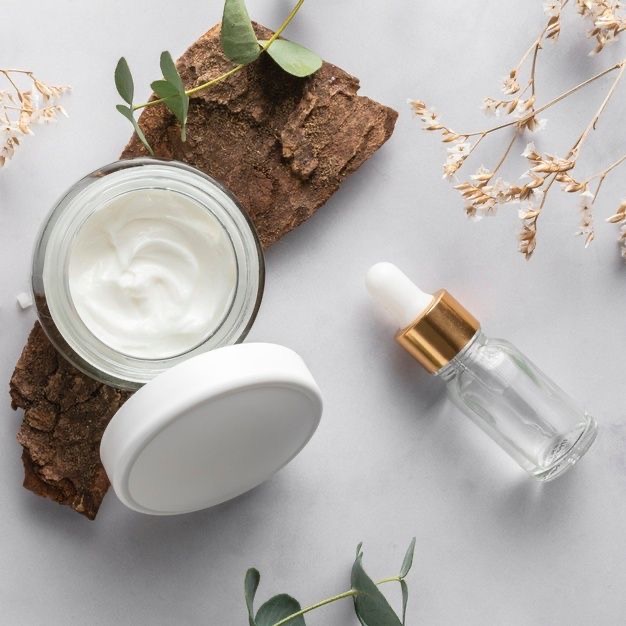 Productos de cosmética natural y vegana con sérum y cremas sobre madera, rodeados de hojas verdes y blancas, estilo elegante y fondo blanco en rst cosmetics.